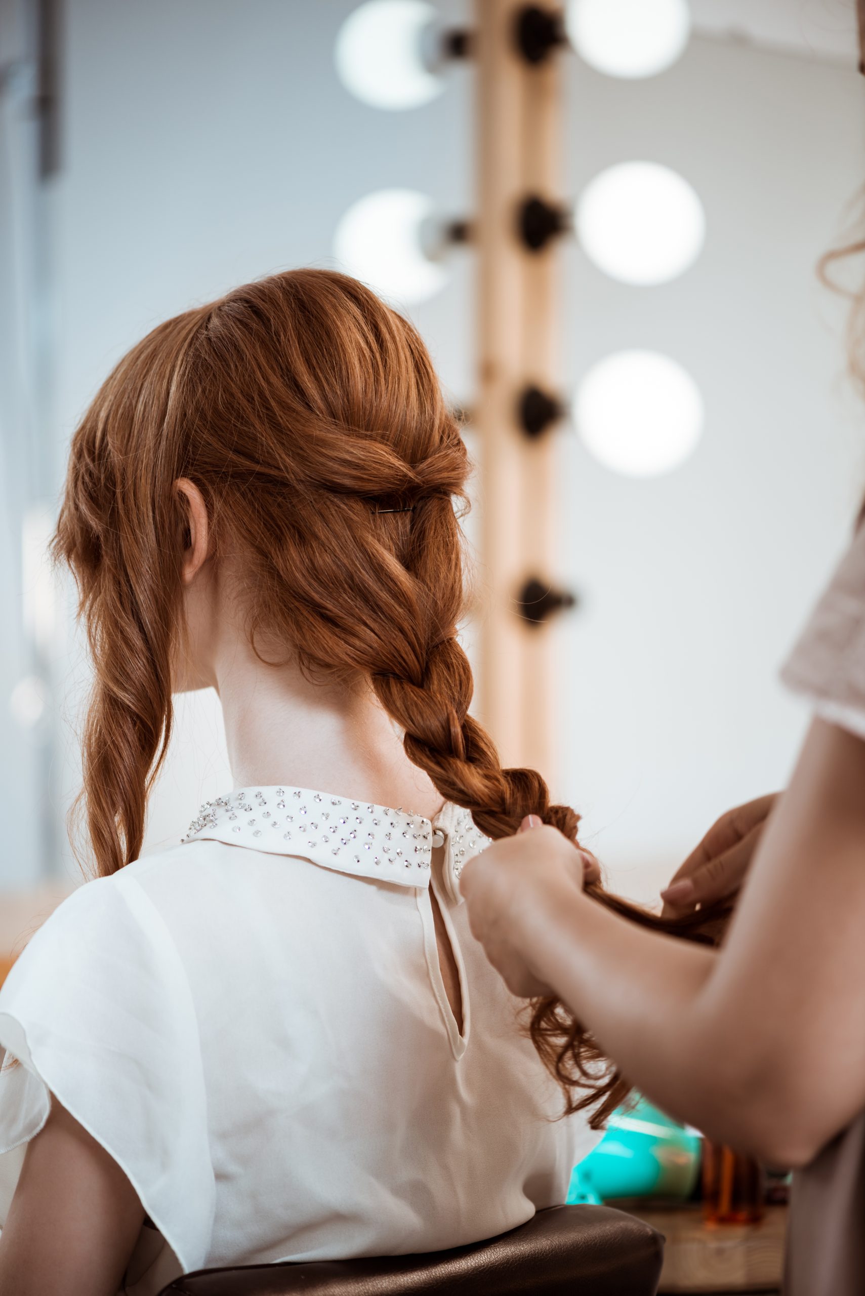Female hairdresser making hairstyle to beautiful redhead girl in beauty salon. Copy space.